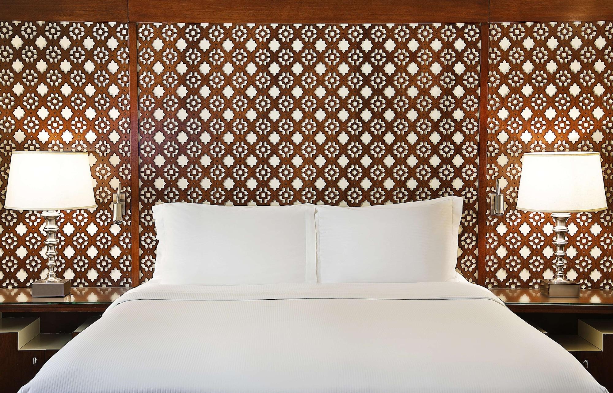 Hilton Suites Jabal Omar Makkah Mekka Exteriér fotografie The image shows a well-appointed bedroom setting with a large, neatly made bed featuring a white duvet and pillows. The headboard is constructed from intricately designed wood, showcasing a geometric pattern that adds an elegant touch to the room. On