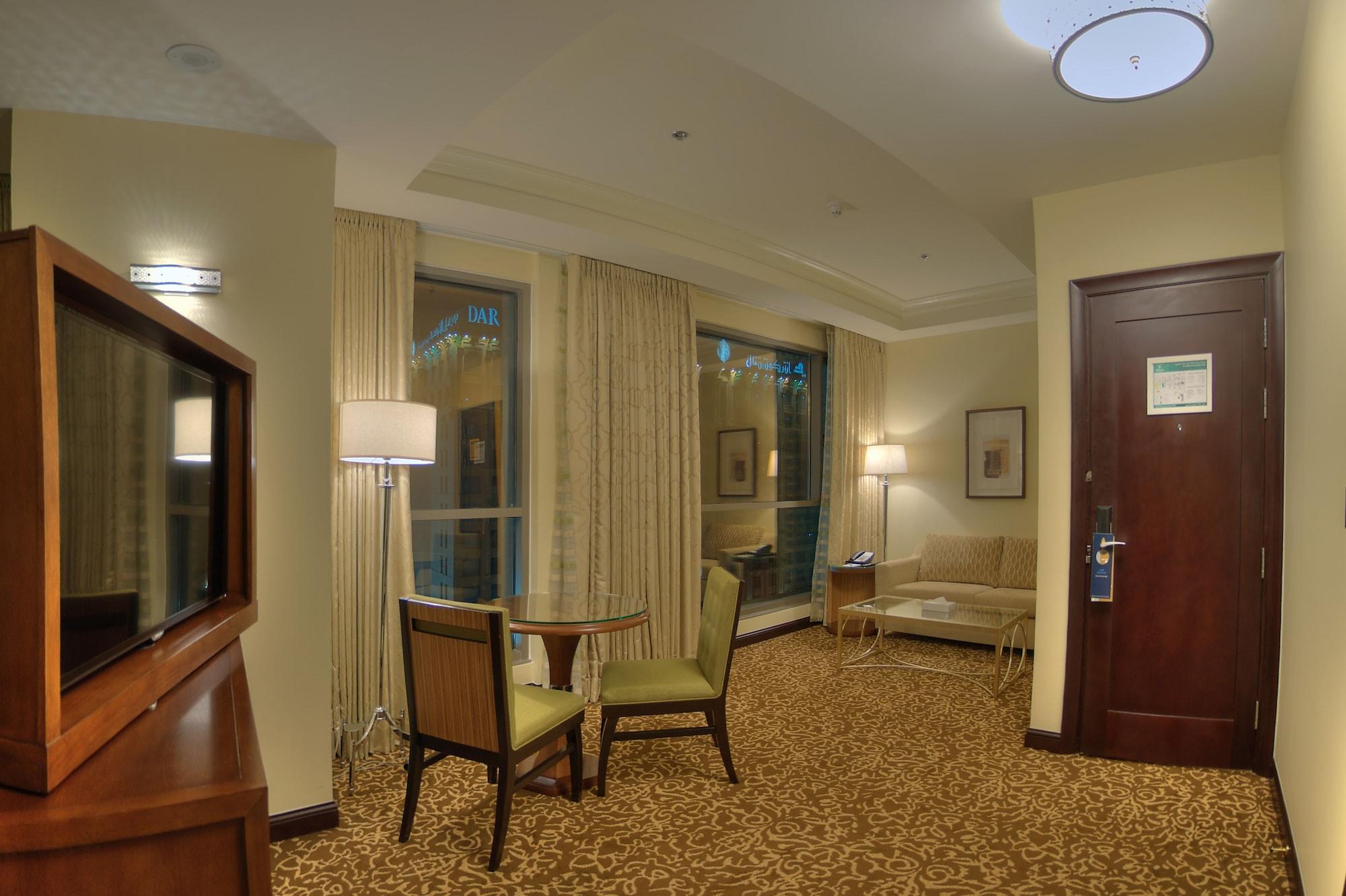 Hilton Suites Jabal Omar Makkah Mekka Exteriér fotografie The photo shows a cozy hotel room or suite that features a small seating area. There is a table with two chairs, suggesting a space for dining or working. A comfortable-looking sofa is positioned against the wall, next to a window covered with light-