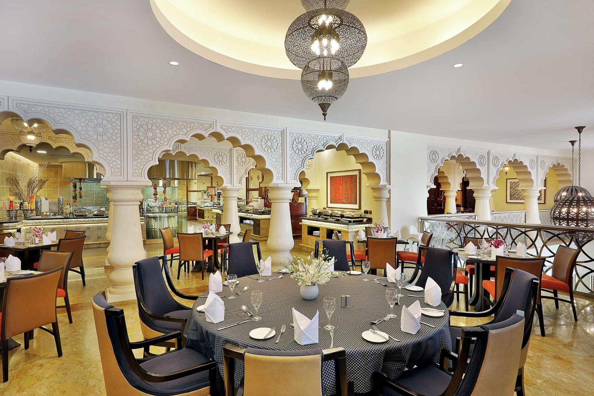 Hilton Suites Jabal Omar Makkah Mekka Exteriér fotografie The photo shows an elegantly designed restaurant interior. The space features a round dining table set with plates, glasses, and folded napkins. Surrounding the table are modern, comfortable chairs. The walls are adorned with intricate architectural 