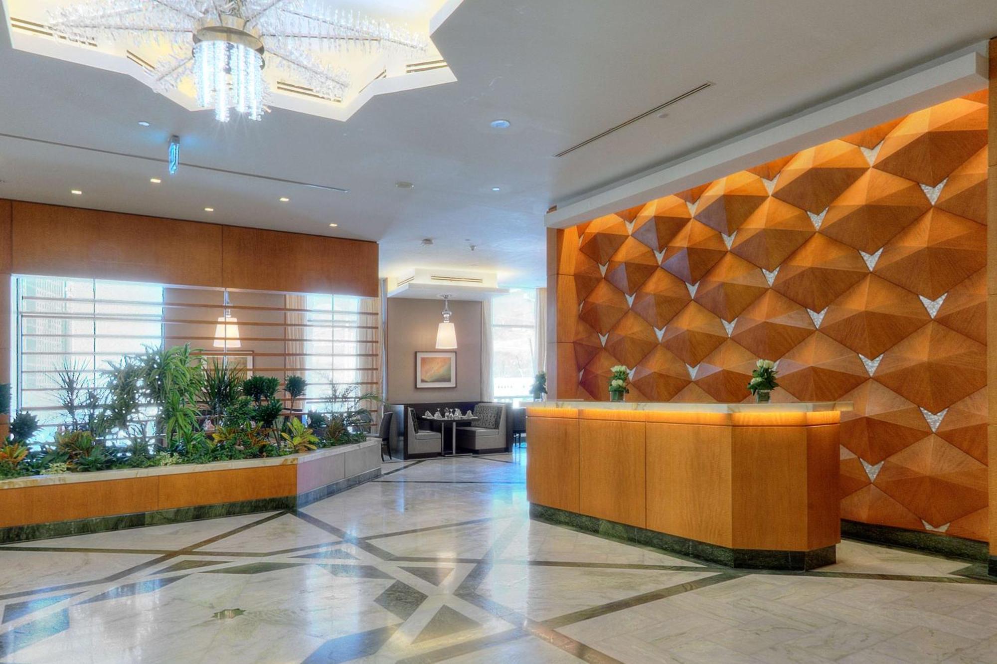 Hilton Suites Jabal Omar Makkah Mekka Exteriér fotografie The photo shows a hotel lobby area. On the right side, there is a reception desk made of wood, featuring a modern design. Behind the desk, there is a decorative wall with a unique geometric pattern in shades of orange and brown. To the left, there ar