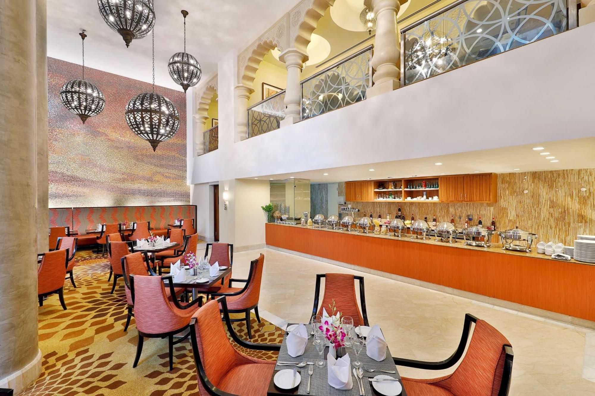 Hilton Suites Jabal Omar Makkah Mekka Exteriér fotografie The photo shows a modern restaurant interior with a spacious and elegant design. It features a dining area with several round tables surrounded by orange chairs. Each table is set with white tableware and adorned with small flower arrangements. 

In 