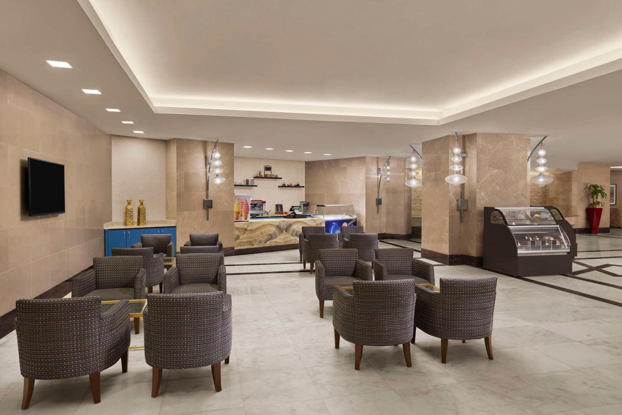 Hilton Suites Jabal Omar Makkah Mekka Exteriér fotografie The photo depicts a modern and inviting lobby area, likely in a hotel or similar establishment. The space features a light-colored tiled floor and beige walls, creating a warm ambiance. 

In the foreground, there are several comfortable armchairs arr